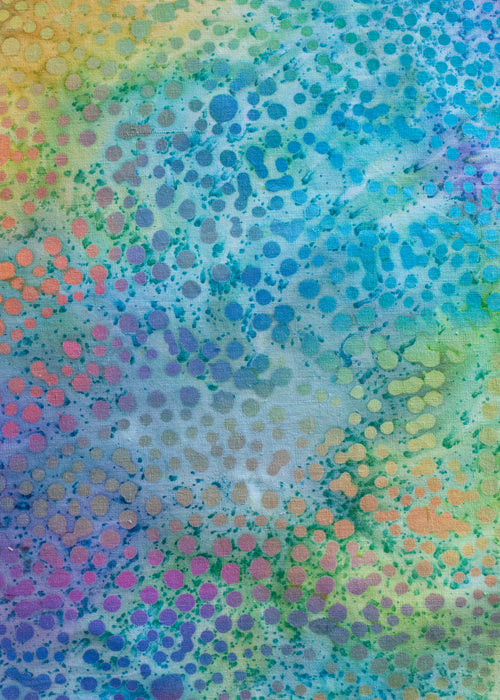 A detail of a kombucha cloth cover with all over dots in gradients of bright colors on a  blue, yellow and green batik background.  