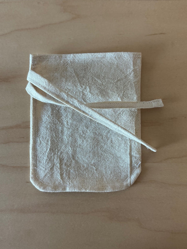 simple cotton reusable teabag with tie closure laying flat on a bright wooden surface. 