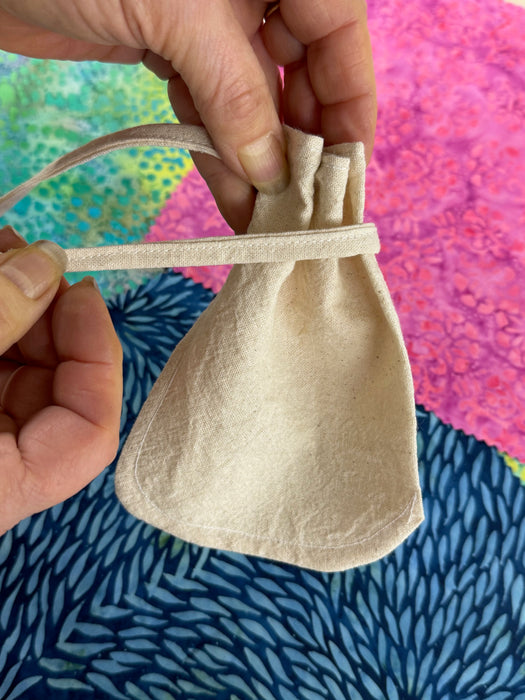 an image with a hand holding a cotton teabag and another holding the tie showing how to gather and tie the tea bag for brewing tea.  